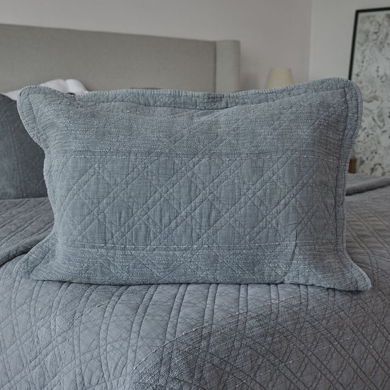 Funda de almohada gris con patrón acolchado diamante sobre cama-