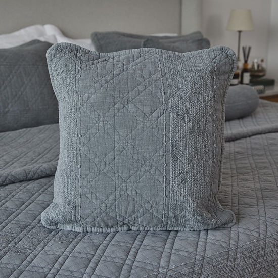 Funda de almohada gris acolchada en cama con edredón coordinado-
