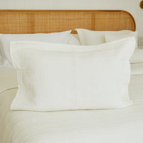 Funda de almohada blanca con textura en cama con cabecero de ratán-natural