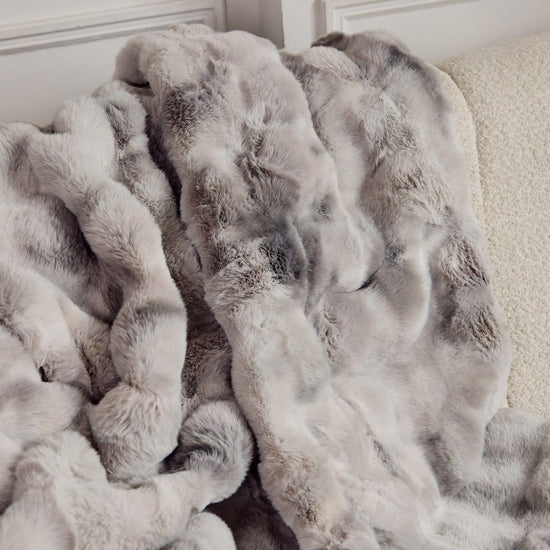Manta suave gris y blanca con textura esponjosa acumulada en sofá-