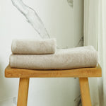 
                    
                      Set de toallas premium beige enrolladas sobre banco de madera-beige
                    
                  