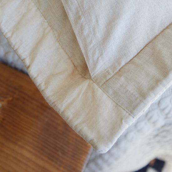 Funda de almohada beige con costuras visibles sobre superficie de madera-beige