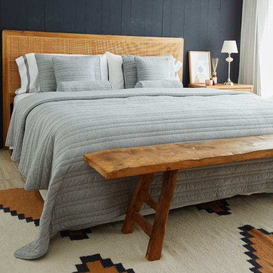 Cama con cabecero de ratán, ropa de cama gris y banco de madera-gris