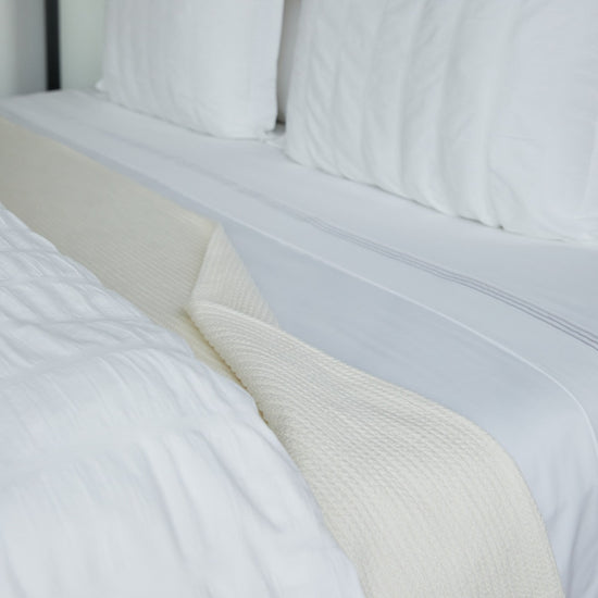 Manta blanca Mykonos sobre cama con almohadas blancas-blanco