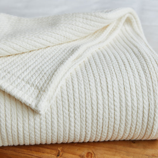 Manta blanca de textura acanalada doblada sobre madera-blanco