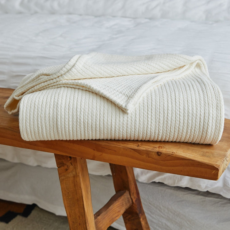 Manta Mykonos blanca de algodón enrollada sobre banco de madera-blanco