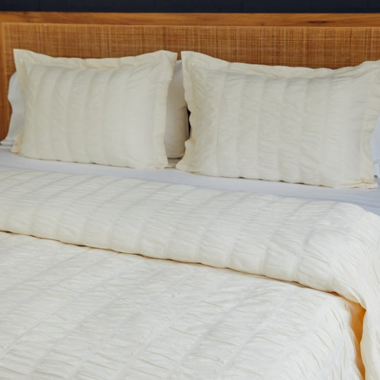 Cama con funda edredón natural, almohadas blancas y cabecero madera-natural
