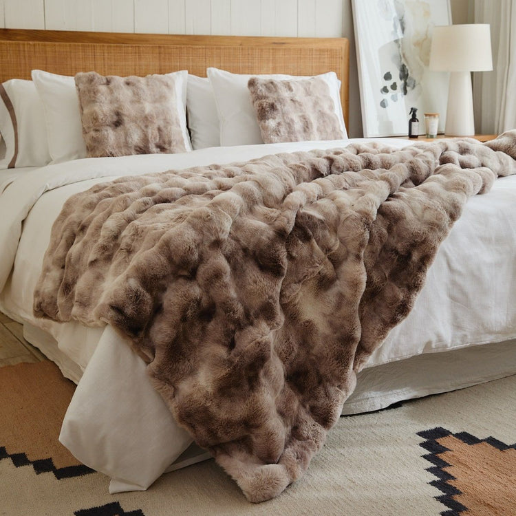 Manta de piel sintética con textura bubble print en tonos beige sobre cama-