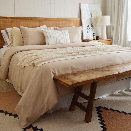 Manta Ginger natural sobre cama con ropa de cama beige y almohadas decorativas-natural