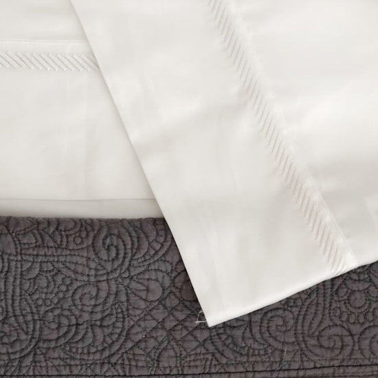 Sábanas blancas de algodón egipcio sobre colcha gris ornamentada-