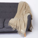 
                    
                      Manta beige con flecos draped sobre sofá gris moderno-
                    
                  