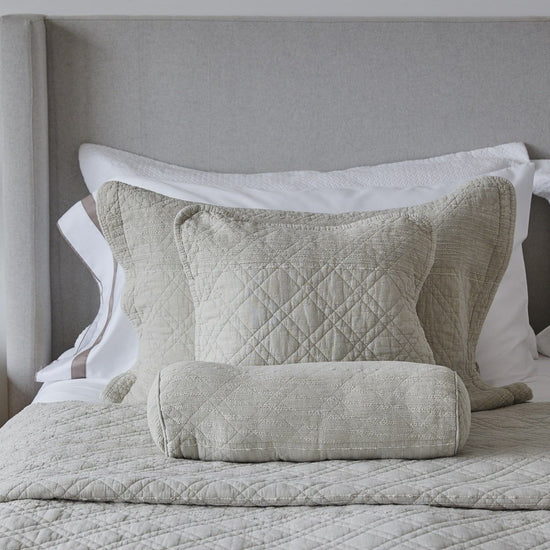 Almohadas decorativas beige y blancas sobre cama con cabecero gris-