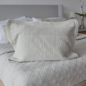 Funda de almohada acolchada color crema sobre cama con cabecero gris-