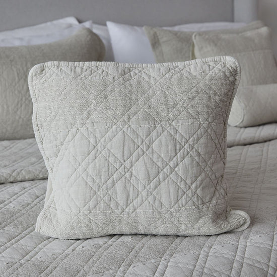 Funda de almohada acolchada beige con patrón de diamantes en cama-