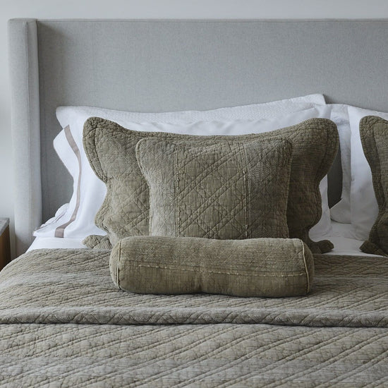 Almohada decorativa con funda verde oliva y ribete blanco en cama-