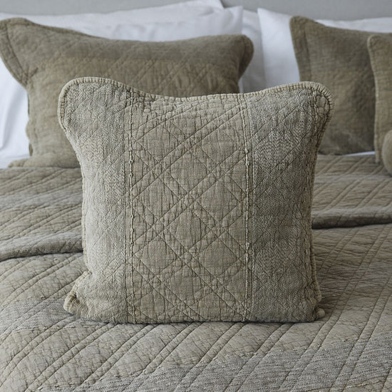 Funda de almohada beige con patrón de rombos acolchado sobre cama-
