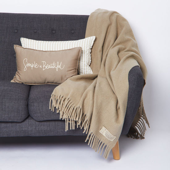 Manta beige con flecos sobre sofá gris con cojines decorativos-beige