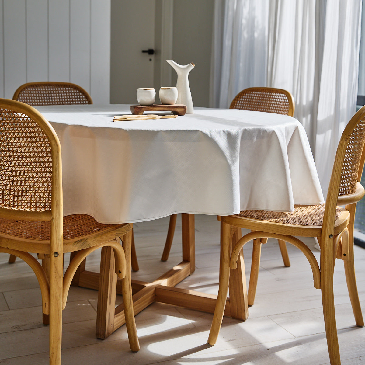Mantel blanco sobre mesa redonda con sillas de madera y ratán-blanco