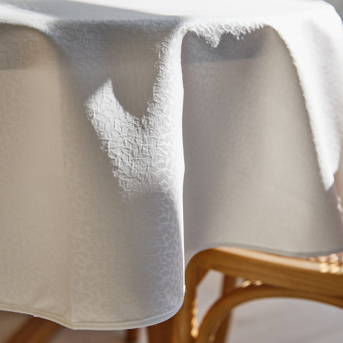 Mantel blanco con pliegues colgado sobre silla de madera clara-blanco