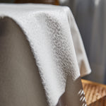 
                    
                      Mantel blanco con textura tejida drapeado sobre mueble de madera-blanco
                    
                  