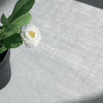 
                    
                      Flor blanca con centro amarillo en jarrón sobre mantel gris-
                    
                  