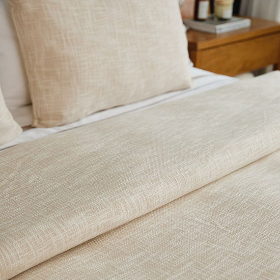 Funda de edredón beige claro sobre cama con almohada y mesita-
