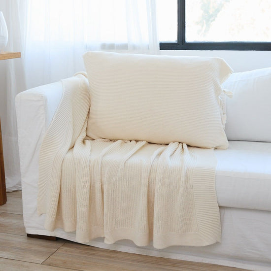Funda de almohada Ginger color crema en sofá blanco junto a ventana-