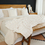 
                    
                      Cama con edredón blanco texturizado y almohadas decorativas en dormitorio elegante-
                    
                  