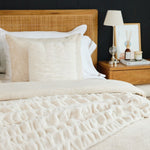 
                    
                      Cama con edredón beige, almohadas y mesita de noche con lámpara-
                    
                  