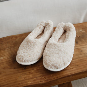 Pantuflas beige de felpa cómoda sobre mesa de madera-