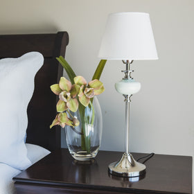 Lámpara de escritorio blanca con base cromada junto a flores amarillas-blanco