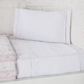 Sábana blanca con motas bordadas en rosa sobre cama-rosa