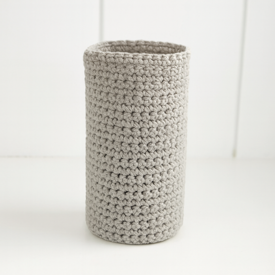 Portabotella cilíndrico de crochet beige texturizado sobre fondo blanco-