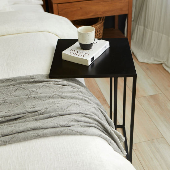Mesa de arrime negro junto a cama con libro y taza de café-negro