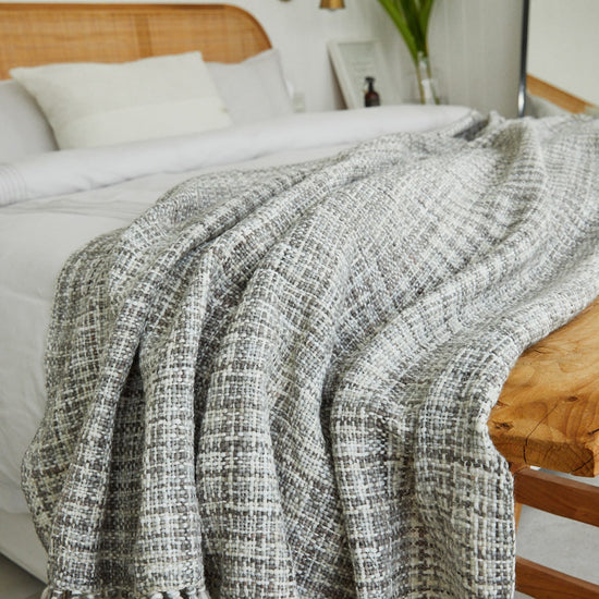 Manta tejida gris clara sobre cama con almohadas blancas y cabecero madera-gris