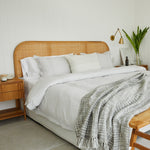 
                    
                      Manta Santorini gris sobre cama con cabecero de ratán y ropa blanca-gris
                    
                  