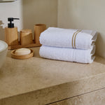 
                    
                      Toallas blancas con líneas beige en encimera de baño con accesorios madera-beige
                    
                  