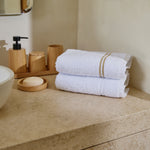 
                    
                      Toallas blancas con rayas beige en encimera de baño con accesorios madera-beige
                    
                  