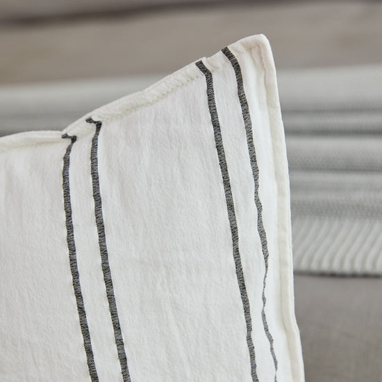 Almohada blanca con rayas grises verticales sobre sofá gris-