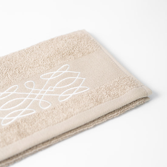 Toalla Viva beige con diseño blanco decorativo sobre fondo neutro-beige